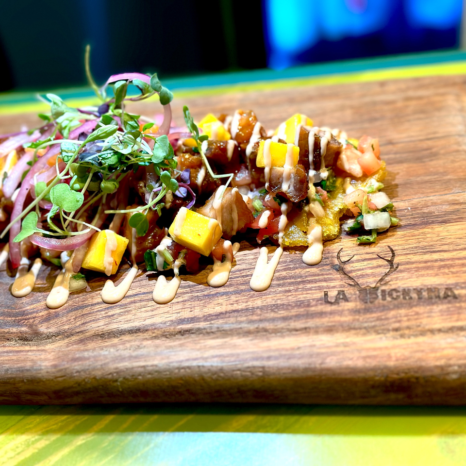 La Vickyna taco with diced mango, red onion, microgreens, and sauce on a wooden board.