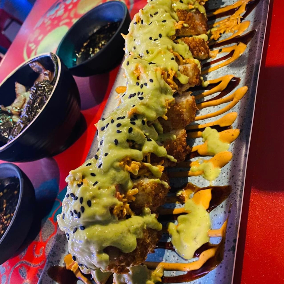 Fried tacos topped with green sauce and black sesame seeds, with two small bowls of sauce.