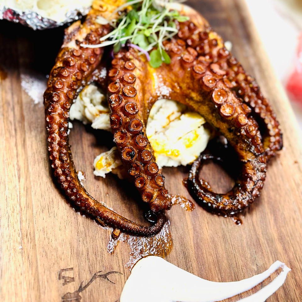 Grilled octopus with mashed potatoes and microgreens, served on a wooden board at La Vickyna.
